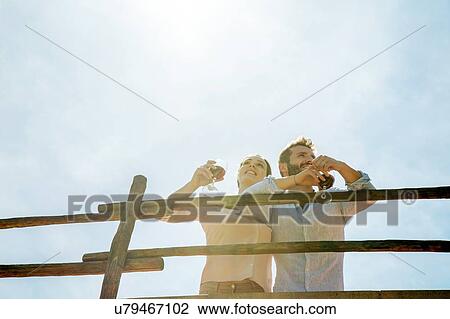 Low angle view of young couple holding wine glasses looking away View Large Photo Image Stock Image - Low angle view of young couple holding wine glasses looking away. Fotosearch