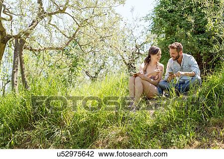Low angle view of young couple sitting on hill holding smartphone View Large Photo Image Stock Image - Low angle view of young couple sitting on hill holding smartphone. Fotosearch