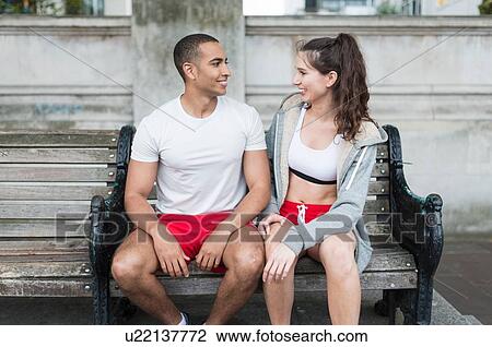 Stock Image - Male and female city runners chatting on bench. Fotosearch