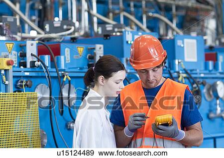 Stock Photo - Male and female colleagues looking down at handheld machine. Fotosearch