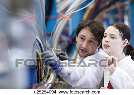 Picture - Male and female colleagues wearing lab coats inspecting wires. Fotosearch