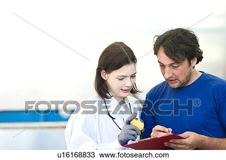 Stock Image - Male and female colleauges looking down inspecting petri dish, writing on clipboard. Fotosearch