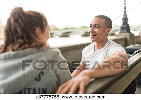 Stock Photograph - Male and female runners chatting on bench, Southbank, London, UK. Fotosearch