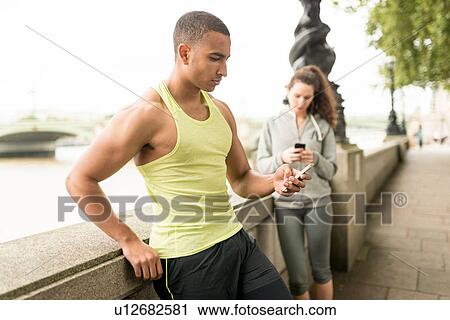 Male and female runners texting on smartphone at riverside View Large Photo Image Stock Image - Male and female runners texting on smartphone at riverside. Fotosearch