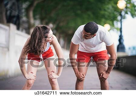 Stock Image - Male and female runners warming up on riverside. Fotosearch