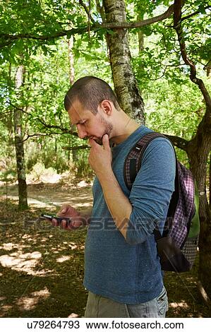 Stock Image - Male hiker looking down at smartphone in forest. Fotosearch