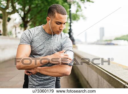 Stock Photo - Male runner choosing smartphone music on Southbank, London, UK. Fotosearch