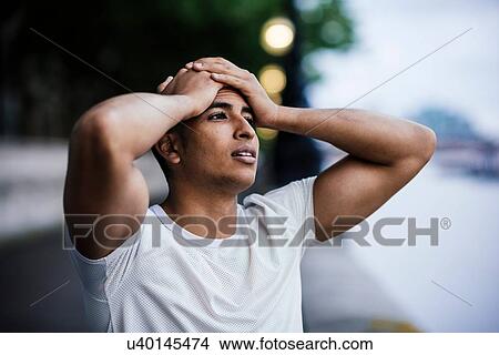 Picture - Male runner with hands on forehead taking a break on riverside. Fotosearch