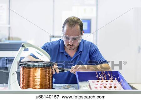 Stock Photo - Male worker assembling electromagnetic coils in electronics factory. Fotosearch