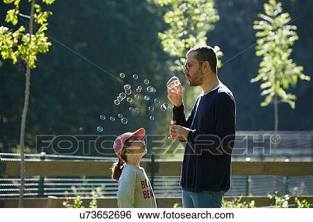 Man blowing bubbles as daughter looks up View Large Photo Image Stock Photograph - Man blowing bubbles as daughter looks up. Fotosearch