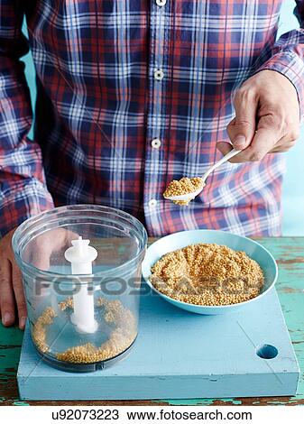 Stock Image - Man preparing fresh mustard recipe step 1, mustard seeds in food processor. Fotosearch