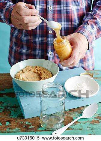 Stock Photography - Man preparing fresh mustard recipe step 2, adding honey to blended mustard seeds. Fotosearch