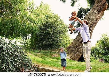 Stock Photography - Mature man lifting up daughter in garden. Fotosearch