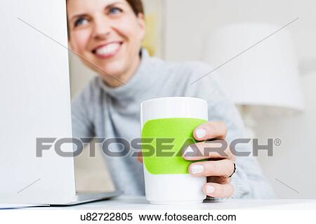 Mature woman at laptop holding cup smiling, focus on foreground View Large Photo Image Stock Photography - Mature woman at laptop holding cup smiling, focus on foreground. Fotosearch