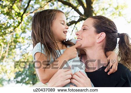 Stock Photo - Mature woman carrying daughter in arms in park. Fotosearch