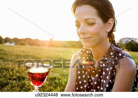 Mature woman contemplating red wine in park View Large Photo Image Stock Photo - Mature woman contemplating red wine in park. Fotosearch