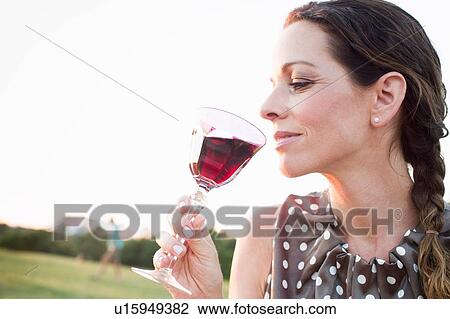 Stock Image - Mature woman drinking glass of red wine in park. Fotosearch