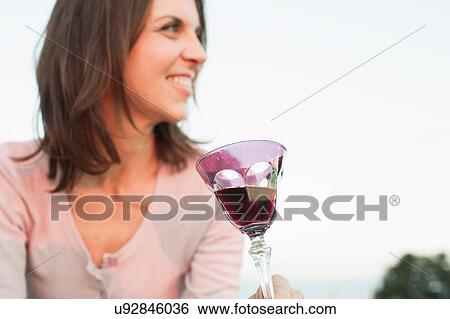 Stock Photograph - Mature woman drinking glass of red wine in park. Fotosearch
