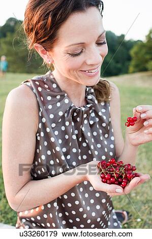 Stock Photo - Mature woman eating redcurrants in park. Fotosearch