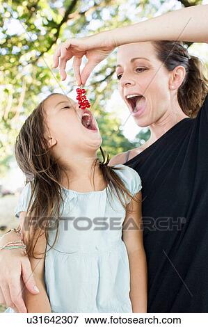Stock Photo - Mature woman feeding daughter redcurrants in park. Fotosearch