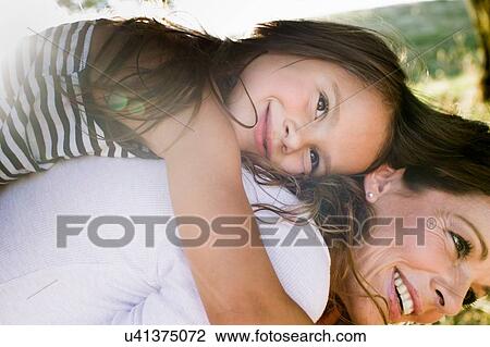 Stock Image - Mature woman giving daughter piggy back in park. Fotosearch