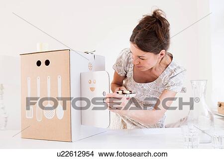 Picture - Mature woman holding baked products looking at cardboard box with kitchen utensil motif. Fotosearch