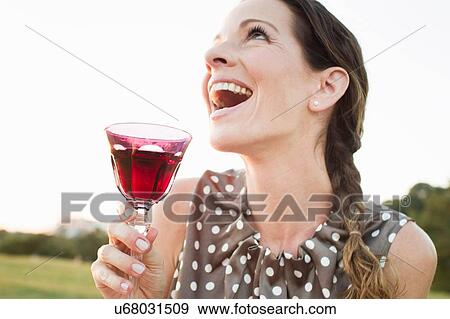Mature woman laughing whilst drinking glass of red wine in park View Large Photo Image Stock Photo - Mature woman laughing whilst drinking glass of red wine in park. Fotosearch