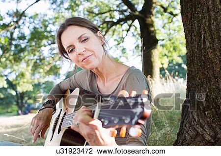 Mature woman playing acoustic guitar in park View Large Photo Image Stock Image - Mature woman playing acoustic guitar in park. Fotosearch