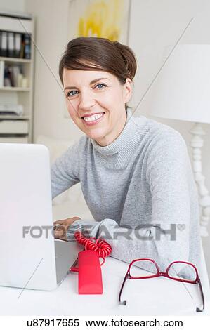 Mature woman sitting at laptop looking at camera smiling View Large Photo Image Stock Photography - Mature woman sitting at laptop looking at camera smiling. Fotosearch