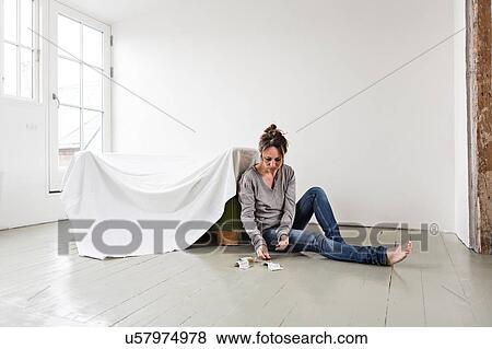 Stock Photo - Mature woman sitting on floor in empty house, counting money. Fotosearch