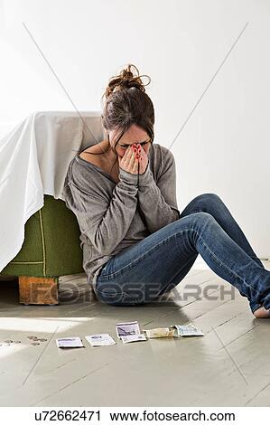 Stock Image - Mature woman sitting on floor in house, counting money, distressed expression. Fotosearch