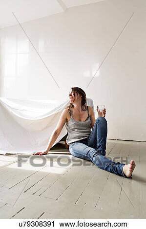 Stock Image - Mature woman sitting on floor in house, pensive expression. Fotosearch