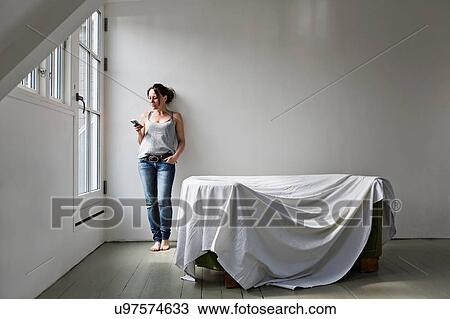 Stock Image - Mature woman standing in part furnished home, using mobile phone. Fotosearch