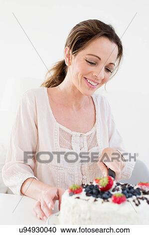 Mature woman using knife to slice fruit covered cake looking down smiling View Large Photo Image Stock Image - Mature woman using knife to slice fruit covered cake looking down smiling. Fotosearch