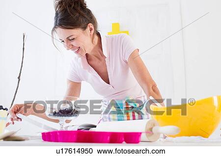 Stock Image - Mature woman wearing apron preparing food looking down smiling. Fotosearch
