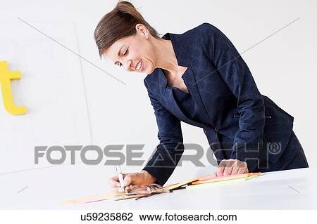 Mature woman wearing business attire writing on paperwork, looking down smiling View Large Photo Image Stock Image - Mature woman wearing business attire writing on paperwork, looking down smiling. Fotosearch