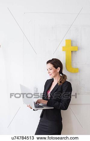 Mature woman wearing business attire standing using laptop View Large Photo Image Stock Image - Mature woman wearing business attire standing using laptop. Fotosearch