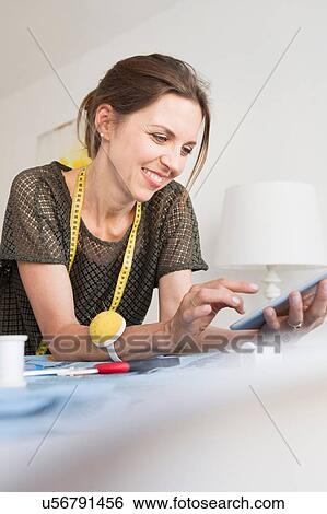 Stock Photograph - Mature woman with tape measure resting on elbows using digital tablet smiling. Fotosearch