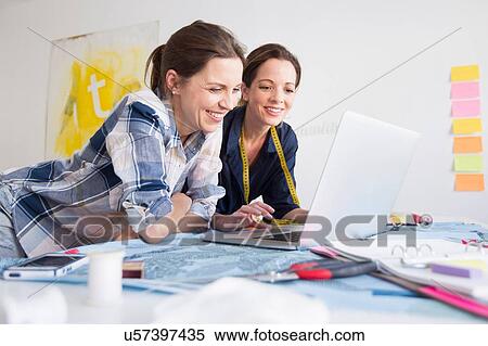 Stock Photography - Mature women at desk resting on elbows using laptop smiling. Fotosearch