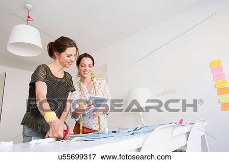 Mature women stand at desk cutting fabric looking at digital tablet View Large Photo Image Stock Photo - Mature women stand at desk cutting fabric looking at digital tablet. Fotosearch