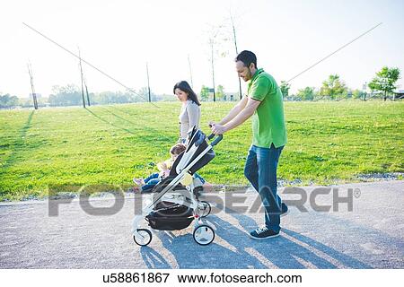 Mid adult couple and toddler daughter in pushchair strolling in park View Large Photo Image Stock Photo - Mid adult couple and toddler daughter in pushchair strolling in park. Fotosearch