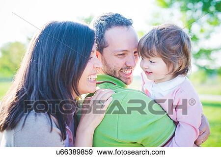 Mid adult couple carrying toddler daughter in park View Large Photo Image Stock Photo - Mid adult couple carrying toddler daughter in park. Fotosearch