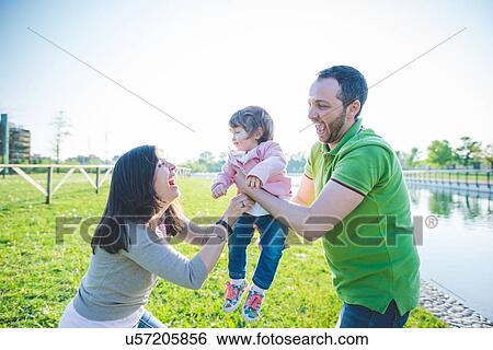 Mid adult couple handing toddler daughter to each other in park View Large Photo Image Stock Photograph - Mid adult couple handing toddler daughter to each other in park. Fotosearch