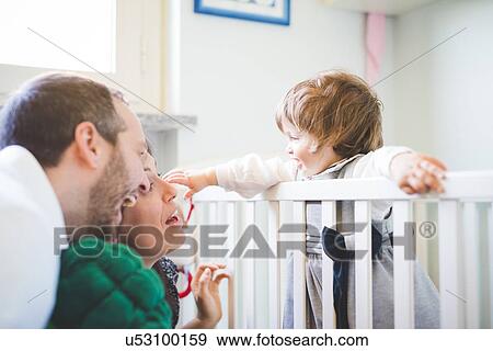Stock Photo - Mid adult couple laughing with toddler daughter in crib. Fotosearch