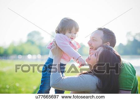 Mid adult couple lifting up toddler daughter in park View Large Photo Image Stock Photo - Mid adult couple lifting up toddler daughter in park. Fotosearch