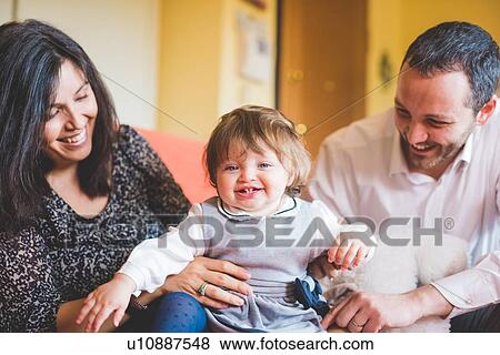 Stock Photo - Mid adult couple playing with toddler daughter on sofa. Fotosearch