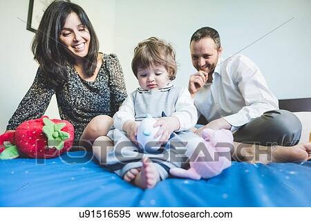 Stock Photography - Mid adult couple playing with toddler daughter on bed. Fotosearch