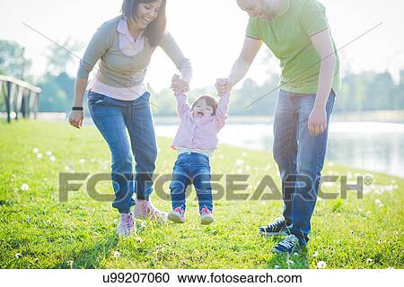 Mid adult couple swinging toddler daughter in park View Large Photo Image Stock Image - Mid adult couple swinging toddler daughter in park. Fotosearch