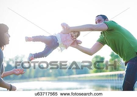 Mid adult couple swinging toddler daughter at riverside View Large Photo Image Stock Photography - Mid adult couple swinging toddler daughter at riverside. Fotosearch