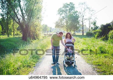 Stock Photography - Mid adult couple with toddler daughter in pushchair strolling in park. Fotosearch